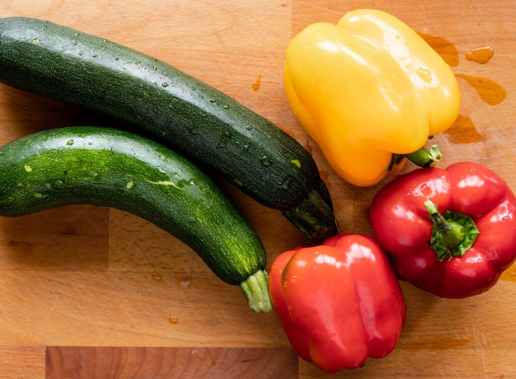 Une exposition vibrante de poivrons et de courgettes sur une surface en bois, mettant en avant leur fraîcheur.