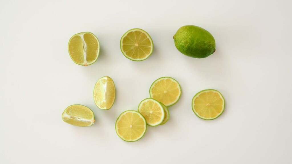 Vue du dessus de tranches de citron vert fraîches et de citrons verts entiers sur une surface blanche. Parfait pour des thèmes alimentaires et de santé.