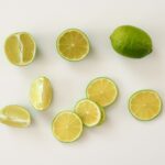Vue du dessus de tranches de citron vert fraîches et de citrons verts entiers sur une surface blanche. Parfait pour des thèmes alimentaires et de santé.