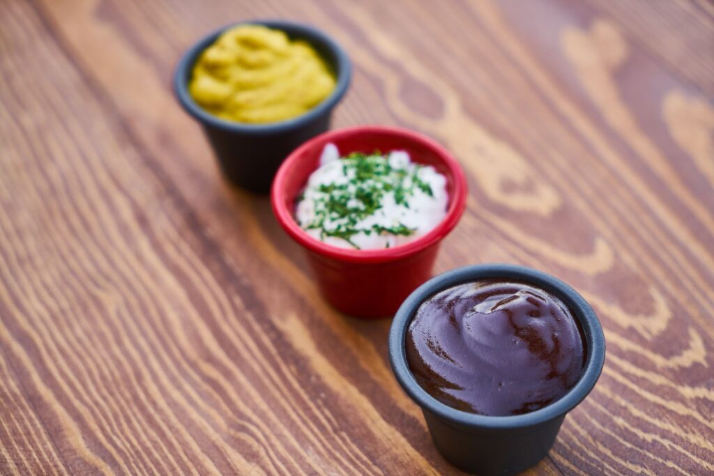 Un gros plan de trois sauces dans des tasses sur une surface en bois, disposées en ligne.