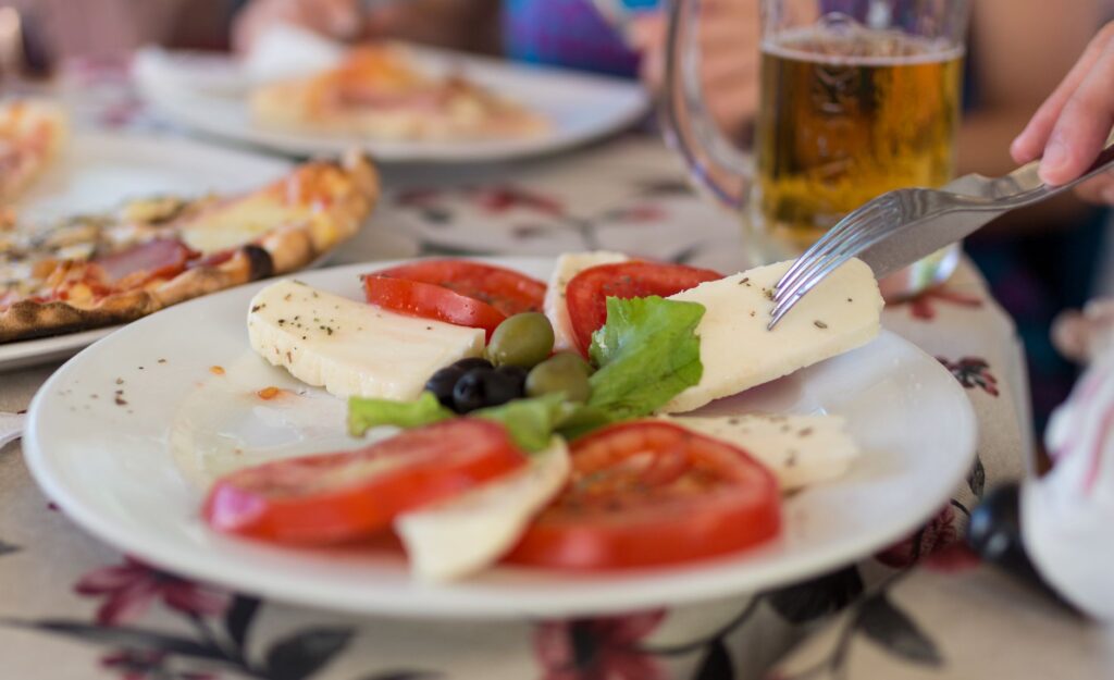 Délicieuse salade caprese italienne avec tomates fraîches, mozzarella et olives servie en plein air avec pizza et bière.