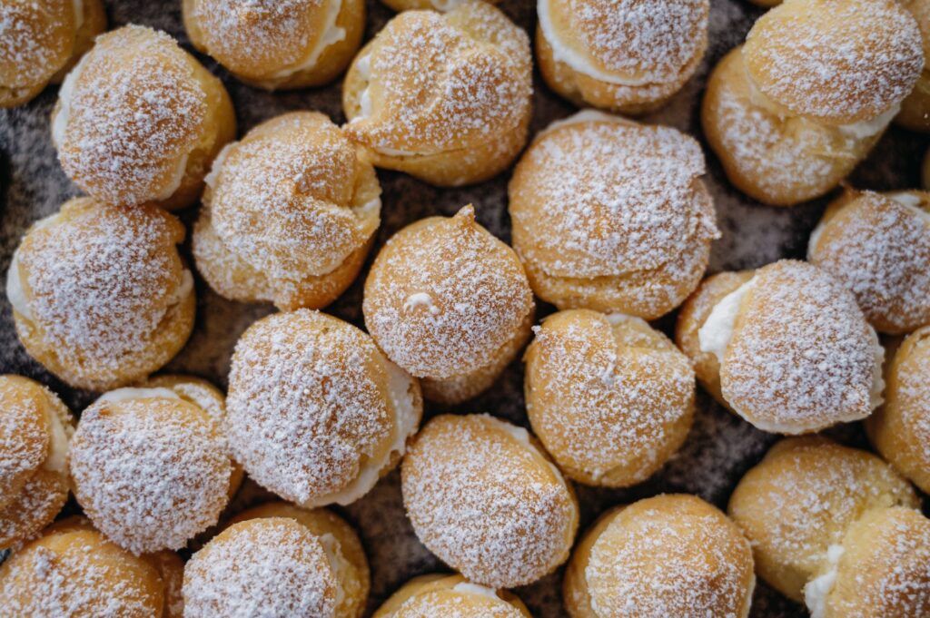 Choux à la crème fraîchement cuits garnis de sucre glace, mettant en valeur un arrangement de desserts délicieux.