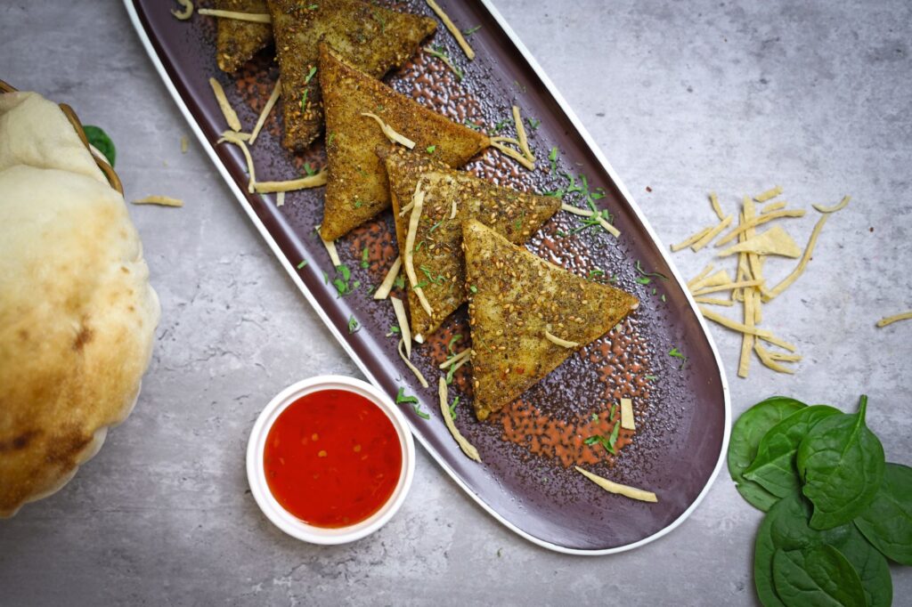 Un plateau de samoussas croustillants servi avec une sauce épicée et des légumes frais.