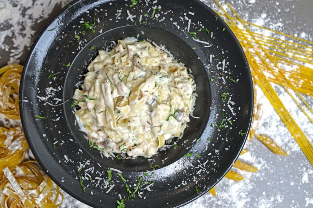 Délicieuses pâtes fettuccine crémeuses garnies de fromage Parmesan et d'herbes sur une assiette noire.