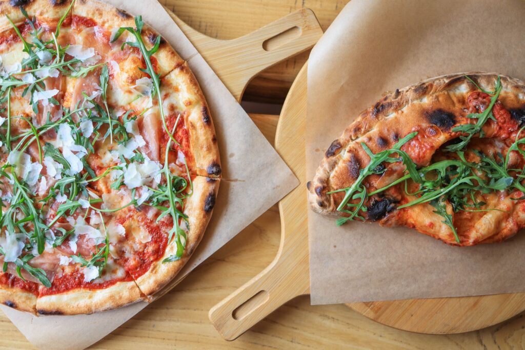 Des pizzas fraîchement cuites garnies de prosciutto, de roquette et de fromage, servies sur des planches en bois.