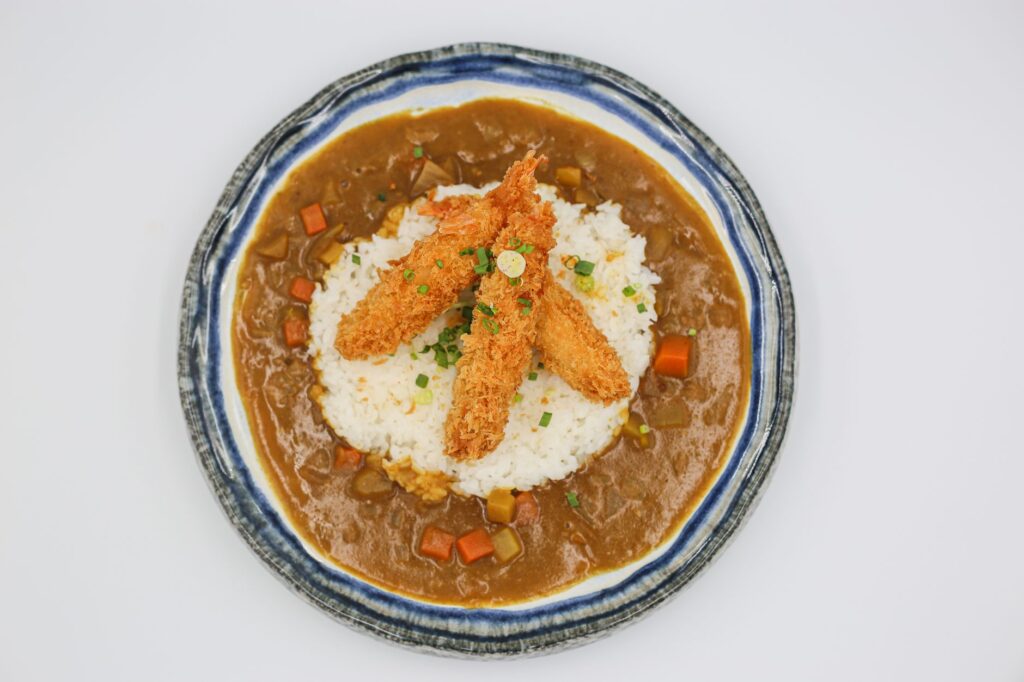Délicieuse ebi tempura servie sur du riz avec une sauce au curry pour un repas japonais savoureux.