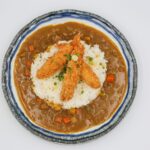 Délicieuse ebi tempura servie sur du riz avec une sauce au curry pour un repas japonais savoureux.