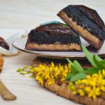 Un délicieux gâteau au chocolat avec une garniture au caramel, servi avec une crème de cacahuète et des fleurs jaunes.
