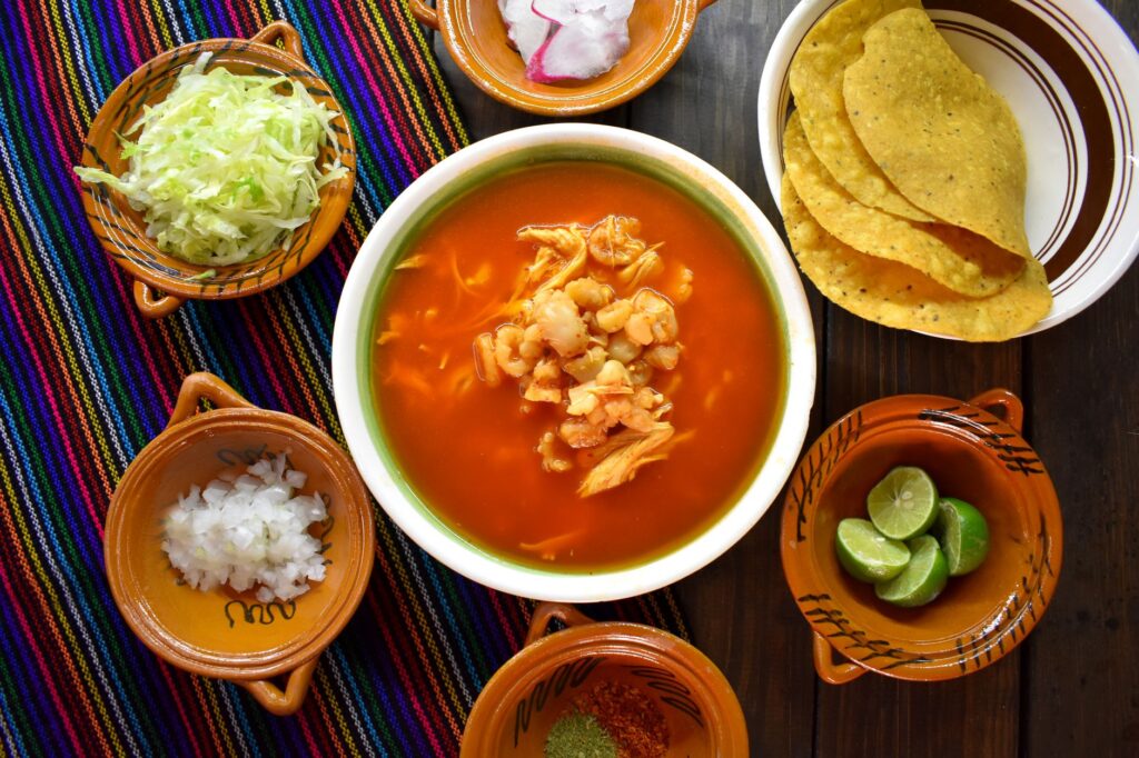 Vue de dessus d'une soupe pozole traditionnelle avec diverses garnitures fraîches, parfaite pour les amateurs de cuisine mexicaine authentique.