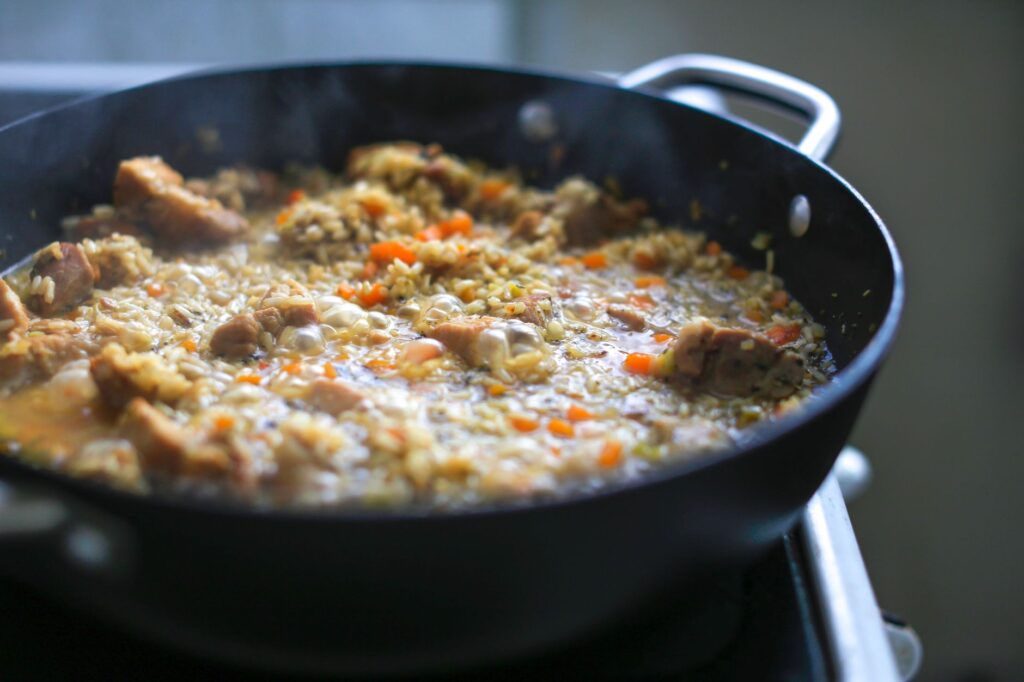 Gros plan sur une paella bouillonnante avec des légumes et de la viande dans une poêle, capturant l'essence des repas faits maison.