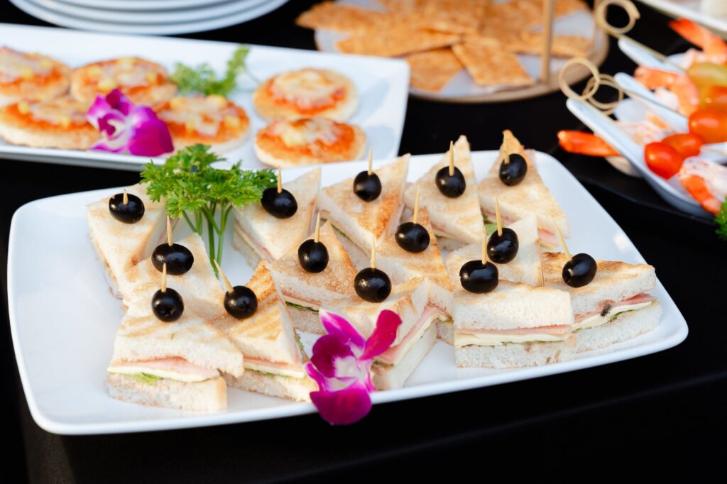 Mise en place élégante d'un banquet avec des sandwiches triangulaires, des olives et des garnitures colorées sur une assiette blanche.