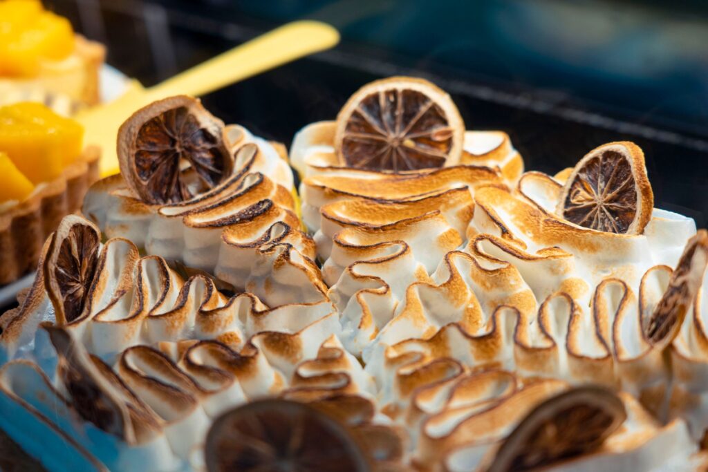 Gros plan sur une tarte au citron meringuée magnifiquement réalisée avec des pics dorés et des tranches de citron séchées, illustrant l'art de la pâtisserie.