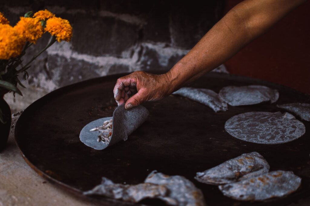 Gros plan sur des mains préparant des tlacoyos en maïs bleu sur une plaque de cuisson, Janitzio, Mexique.