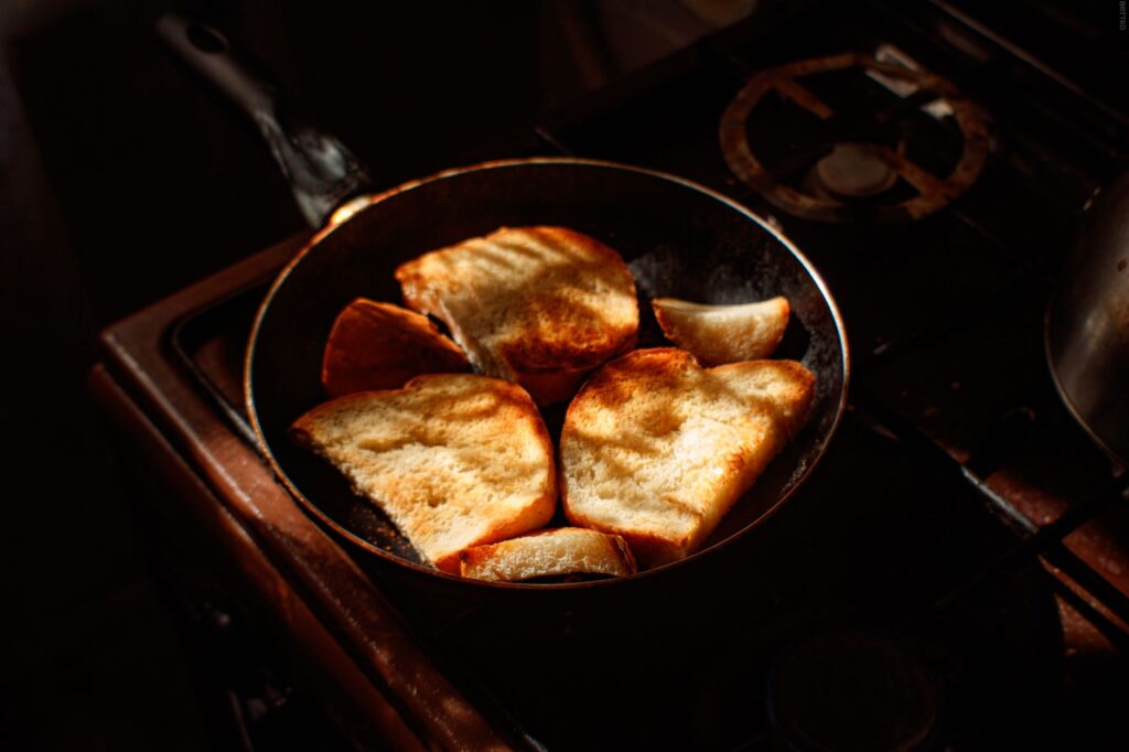 Des toasts dorés cuisinent dans une poêle sur une cuisinière sous une lumière chaleureuse.