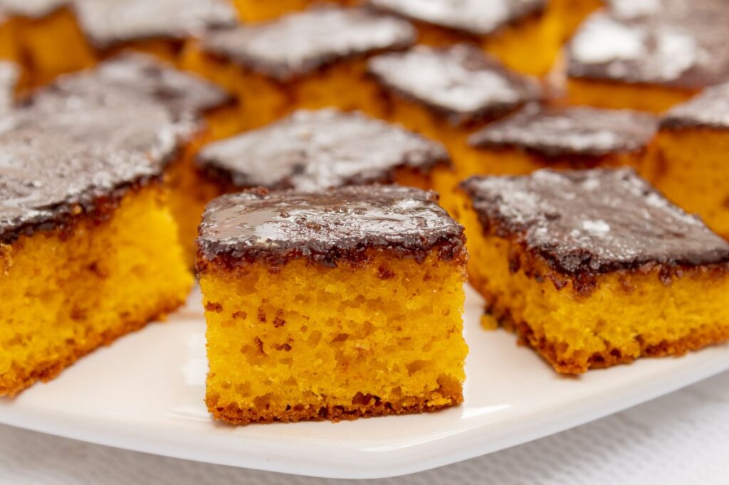 Gros plan sur des carrés de gâteau aux carottes moelleux nappés de glaçage au chocolat, présentés sur une assiette blanche.