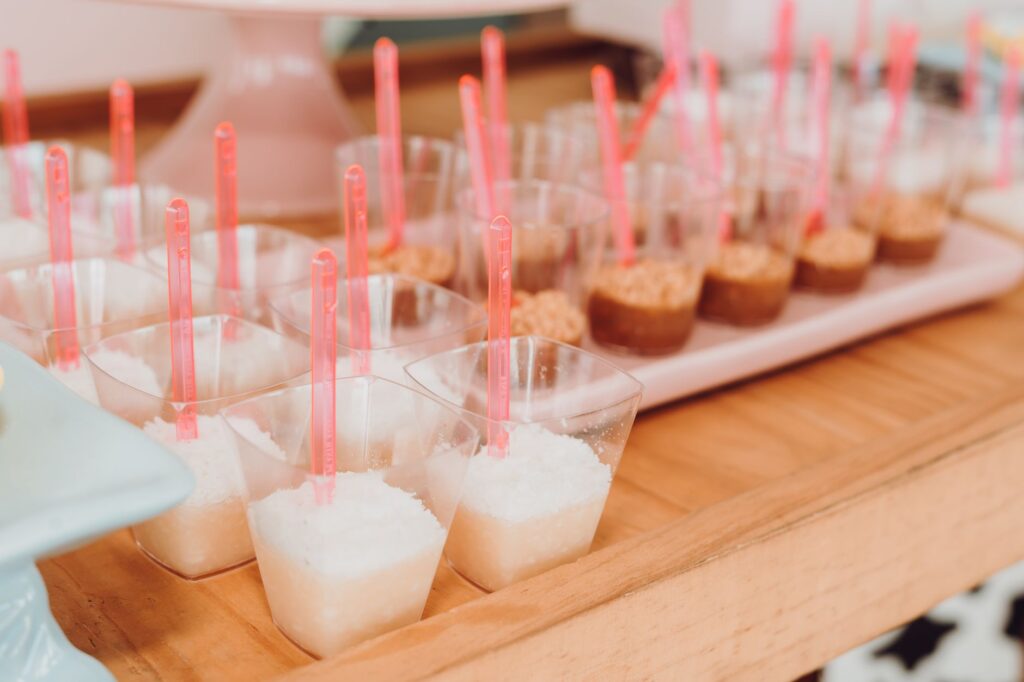 Assortiment de mini desserts dans des gobelets transparents avec des cuillères roses, parfait pour les événements de restauration.