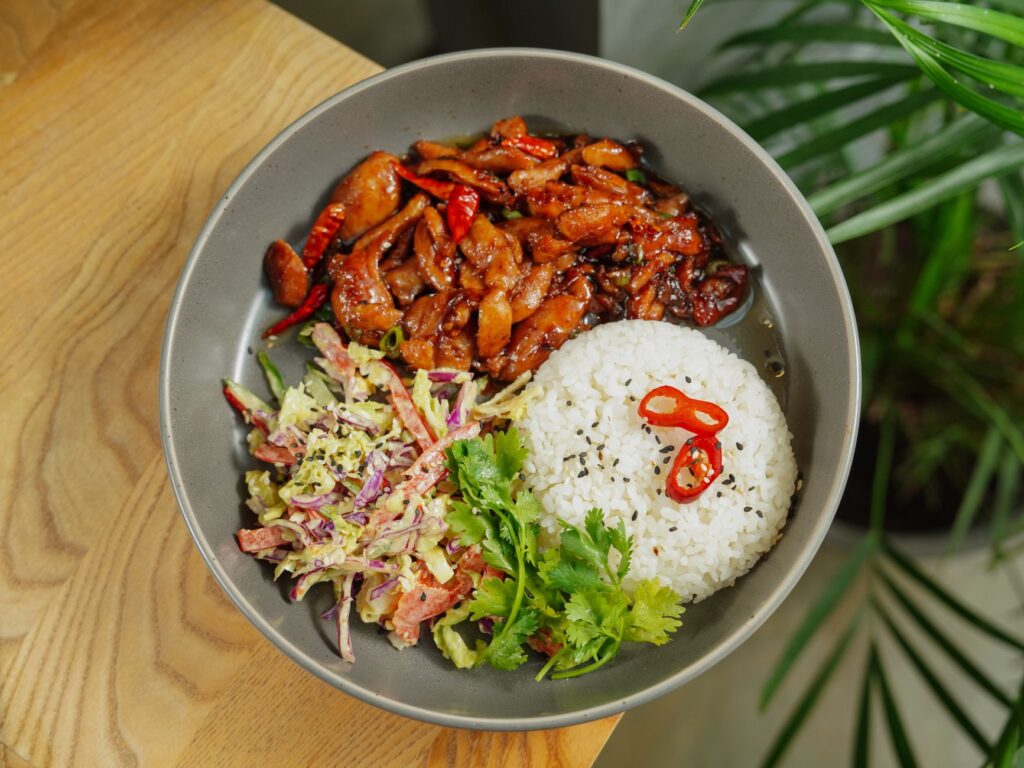 Un plat fusion asiatique vibrant avec du riz, du poulet grillé, une salade et des garnitures.