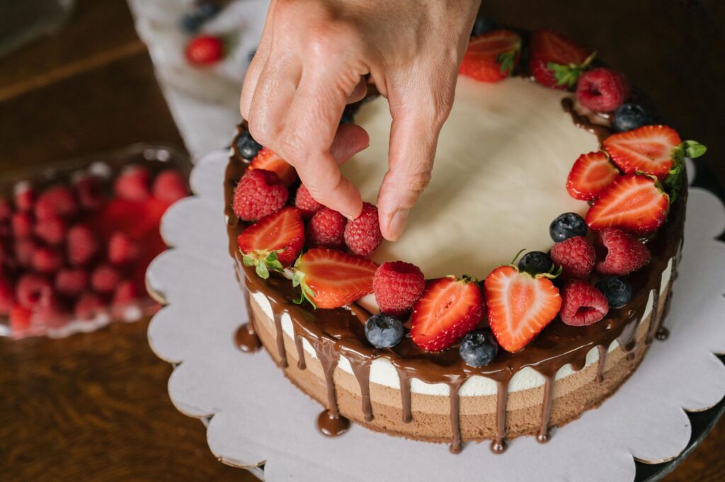 Main plaçant des baies fraîches sur un gâteau couvert de chocolat, créant un délicieux dessert.