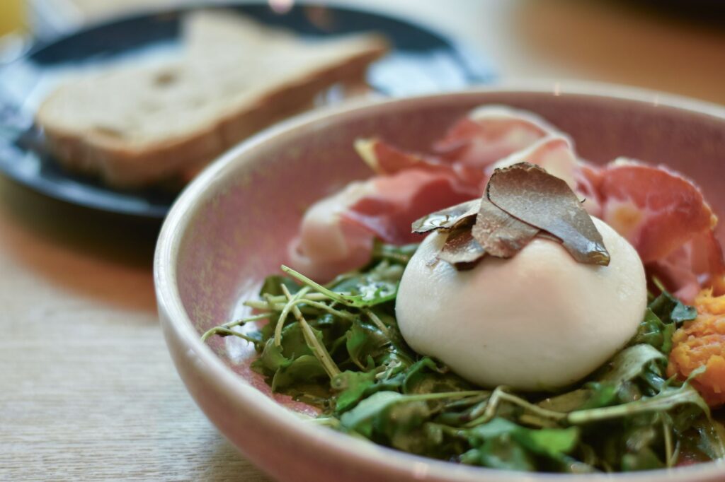 Une délicieuse salade de burrata gourmet avec de la roquette, du prosciutto et des copeaux de truffe, parfaite pour un brunch haut de gamme.