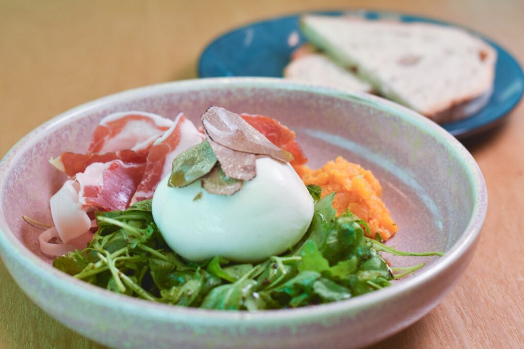 Délicieuse salade de burrata gourmet avec du prosciutto, de la roquette et des copeaux de truffe servie dans un bol en céramique.