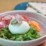 Délicieuse salade de burrata gourmet avec du prosciutto, de la roquette et des copeaux de truffe servie dans un bol en céramique.