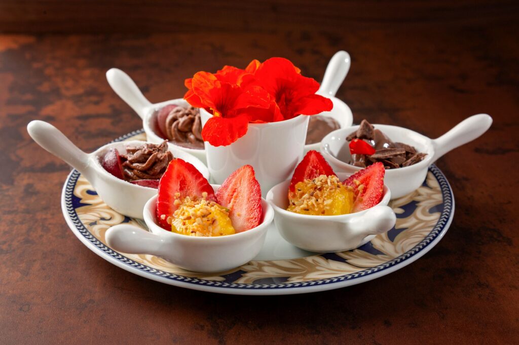 Une assiette de dessert joliment arrangée avec des fraises, des chocolats et des fleurs éclatantes.