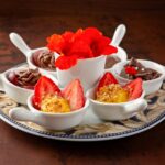 Une assiette de dessert joliment arrangée avec des fraises, des chocolats et des fleurs éclatantes.