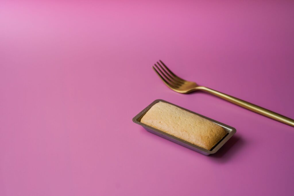 Une fourchette dorée et un dessert rectangulaire sur un fond violet vif.