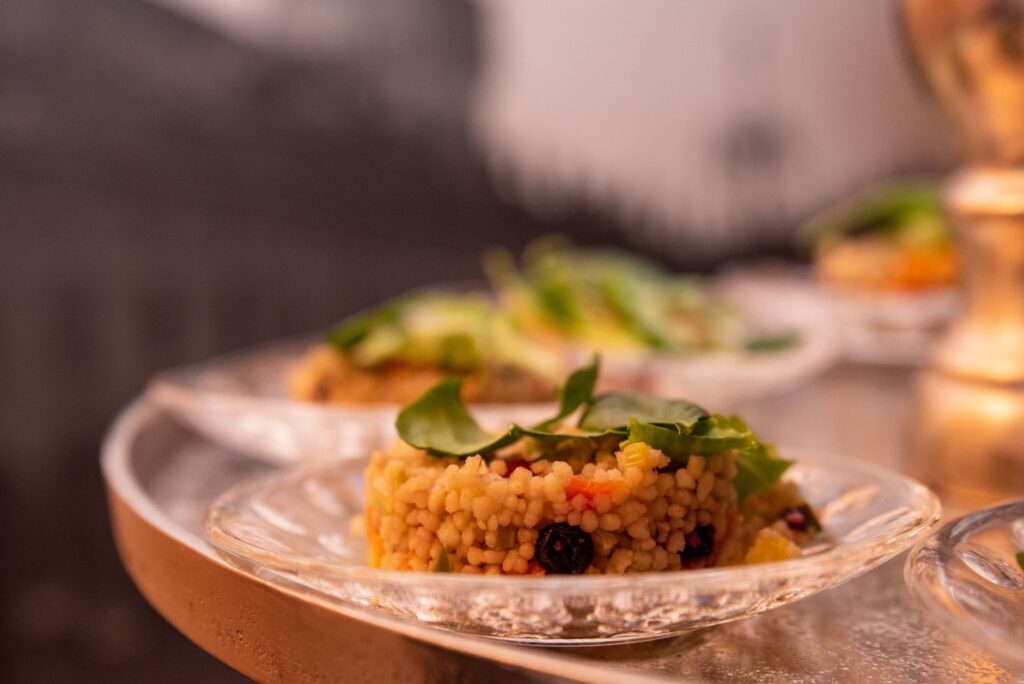 Délicieuses pâtes fregola sur une assiette en verre transparent, garnies de légumes verts.