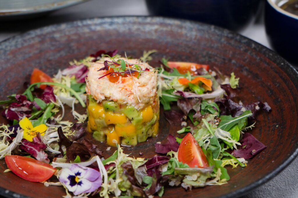 Une salade de crabe gourmet colorée servie avec des légumes frais et de la mangue sur une assiette rustique.