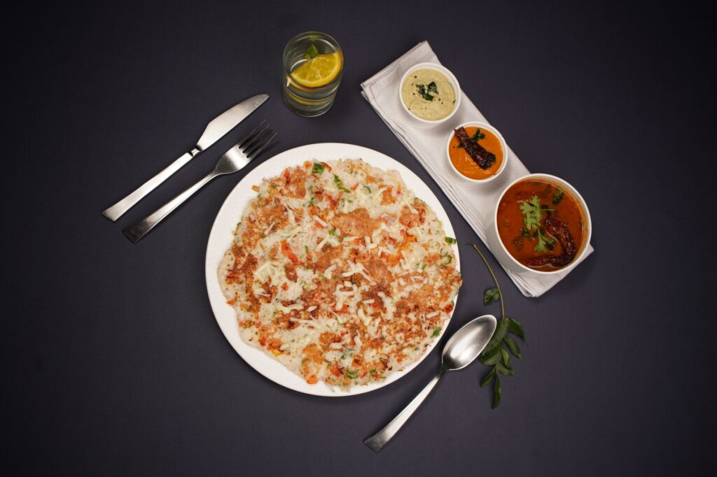 Vue de dessus d'un dosa sud-indien servi avec divers chutneys sur fond noir.