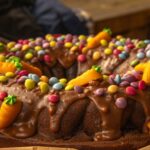 Gros plan sur un gâteau Bundt au chocolat décoré de bonbons colorés et de glaçage, parfait pour les célébrations festives.