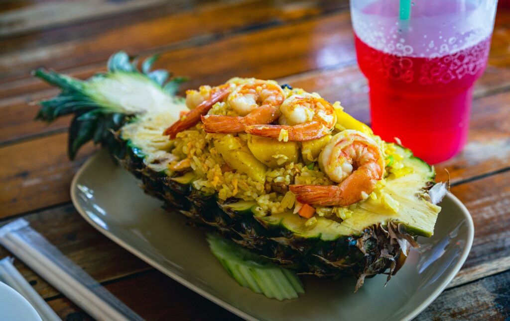 Délicieux riz frit thaïlandais à l'ananas avec des crevettes servi dans une coque d'ananas avec une boisson gazeuse rouge à côté.