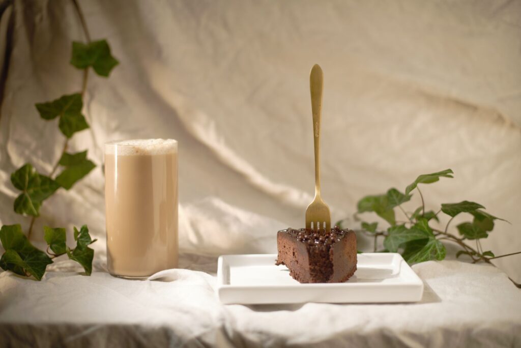 Une tranche de gâteau au chocolat avec un verre de café mousseux, accompagnée de feuilles de lierre dans une disposition rustique.