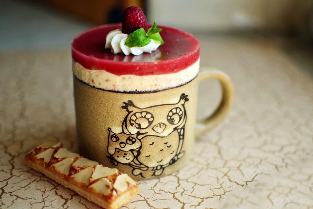 Dessert appétissant avec un glaçage à la framboise servi dans une tasse en forme de hibou, parfait pour une douce indulgence.
