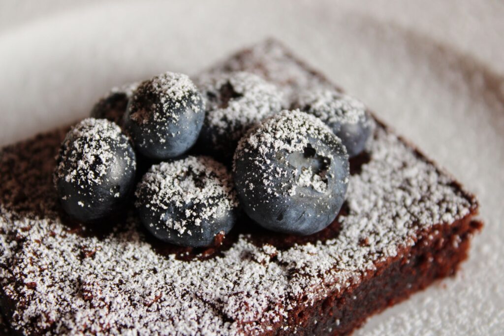Délicieux brownie au chocolat garni de myrtilles fraîches et de sucre glace.