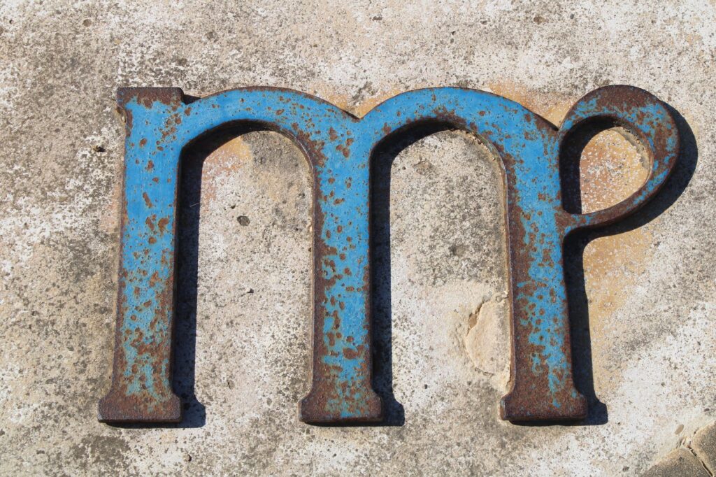 Gros plan sur une lettre en métal bleu rouillée sur un fond en béton texturé, mettant en valeur la décadence et la texture.