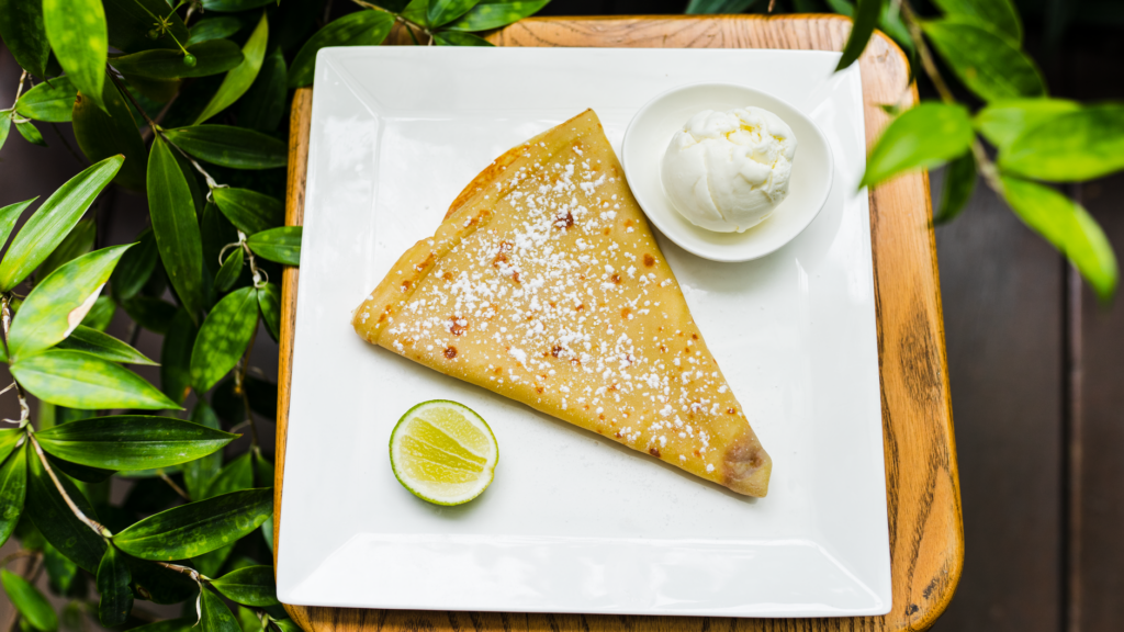 Crêpe servie avec de la crème glacée et une tranche de citron vert sur une assiette carrée, vue de dessus.