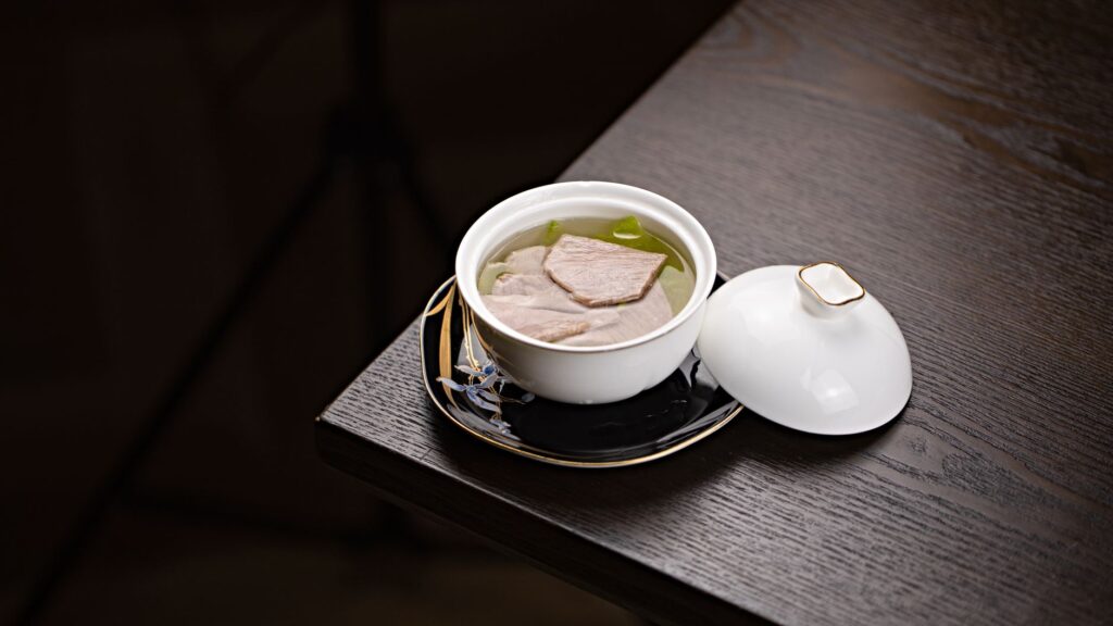 Soupe gastronomique luxueuse avec morceaux de viande dans un plat élégant noir et or, parfait pour la photographie culinaire.