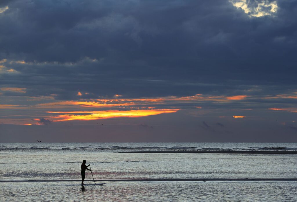 Silhouette d'un paddle boarder pendant le lever du soleil à St. Simons Island, Georgia.