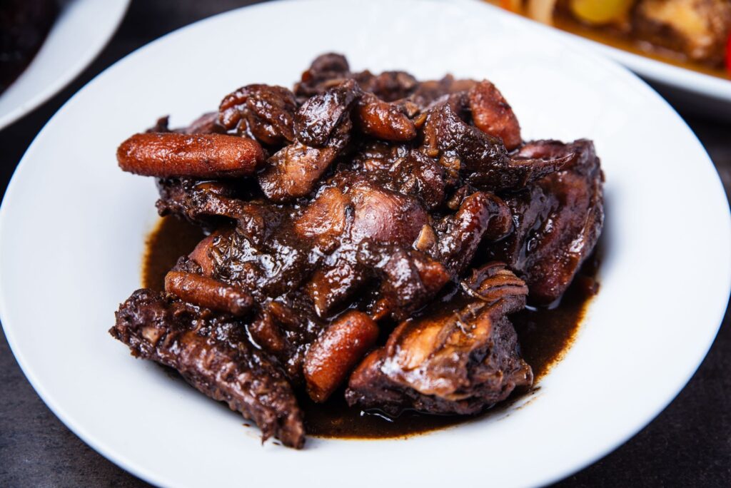 Gros plan sur un plat de canard braisé savoureux accompagné de carottes dans une sauce foncée et parfumée.