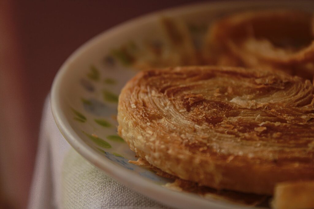 Image chaleureuse en gros plan d'une pâtisserie dorée et feuilletée sur une assiette à motif, idéale pour des thèmes de petit déjeuner.