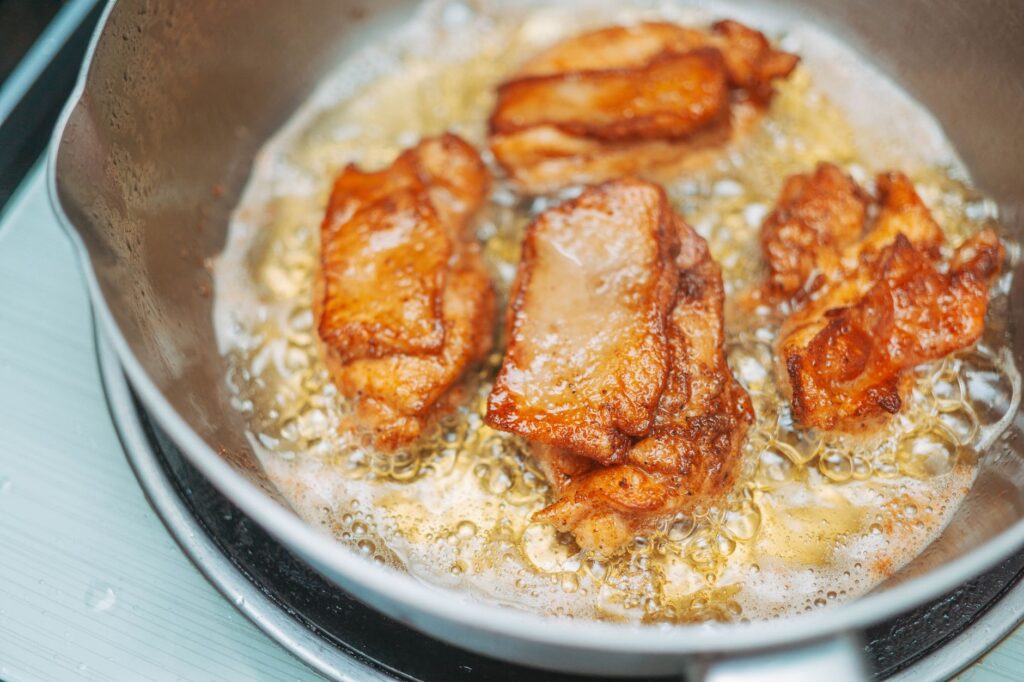 Gros plan de morceaux de poulet frit dorés crépitant dans une poêle chaude pour un repas délicieux.