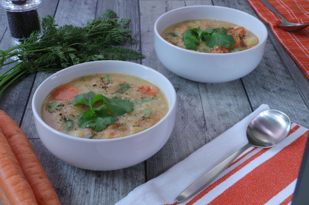 Des bols blancs remplis de soupe de légumes maison copieuse, garnis de coriandre.