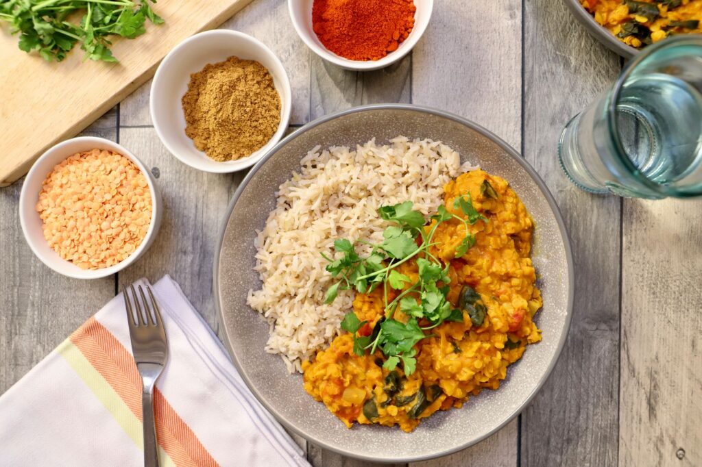 Curry de lentilles vegan savoureux servi avec du riz, garni d'herbes fraîches.