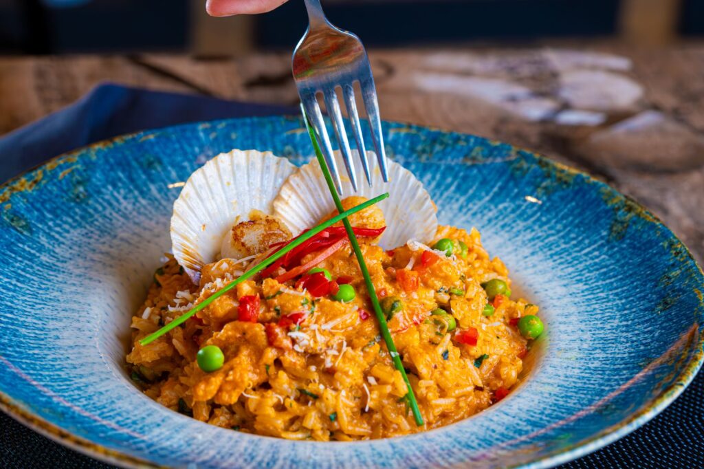 Risotto de fruits de mer vibrant avec des pétoncles et des légumes dans un bol en céramique bleu.