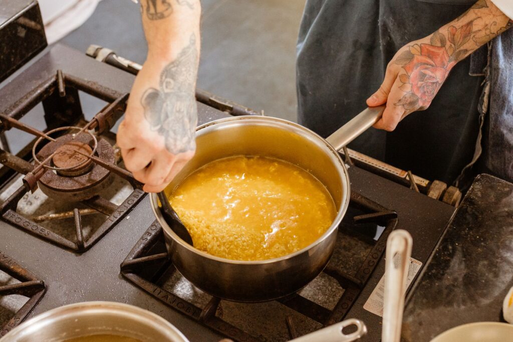 Chef tatoué remuant des pâtes sur une cuisinière tout en cuisinant dans une cuisine.