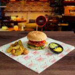 Burger gourmet avec frites et sauce dans un cadre de café élégant, parfait pour les amateurs de bonne cuisine.