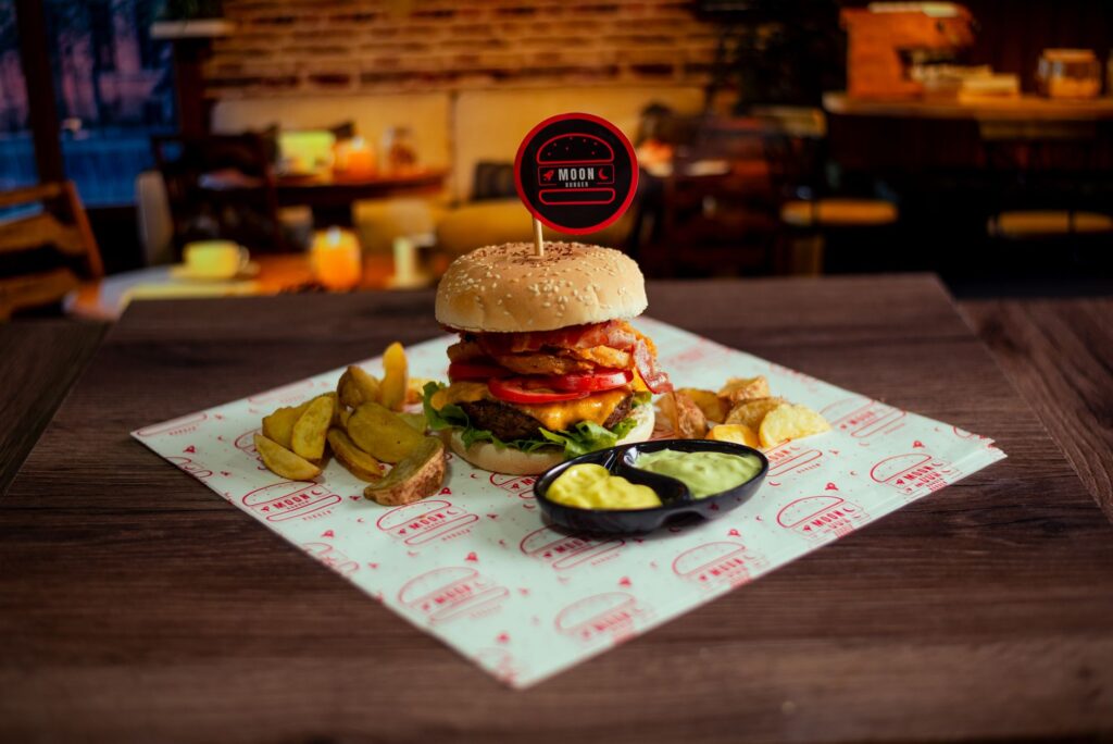 Un burger gourmet qui met l'eau à la bouche, accompagné de wedges croustillants et de sauce, dans un cadre de restaurant accueillant.