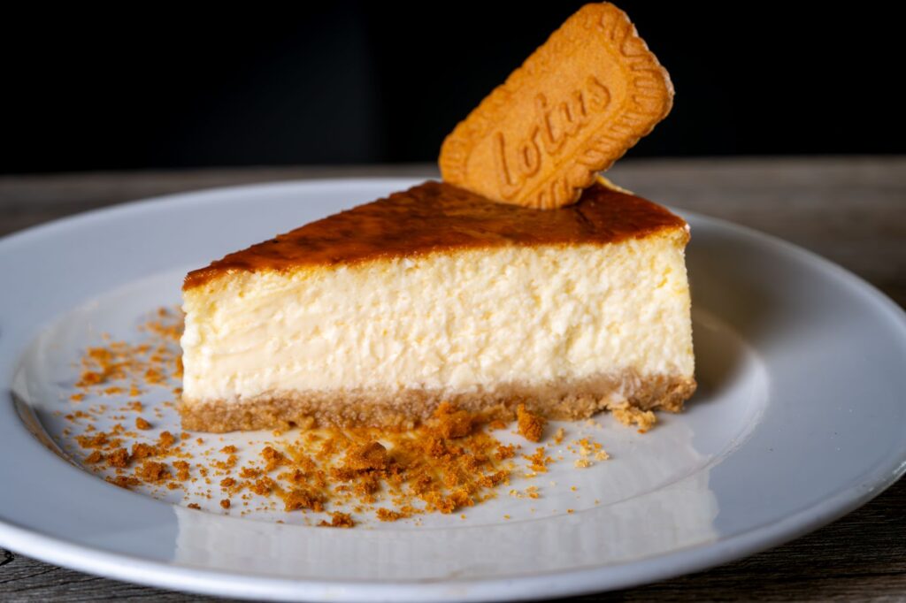 Une tranche de cheesecake crémeux surmontée d'un biscuit Lotus dans une assiette blanche.